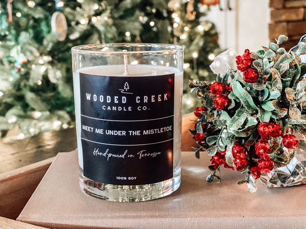 Product image of "Meet Me Under the Mistletoe" candle and mistletoe with tree in back