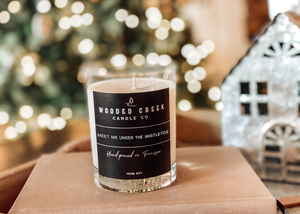 Product image of "Meet Me Under the Mistletoe" candle on table with lights